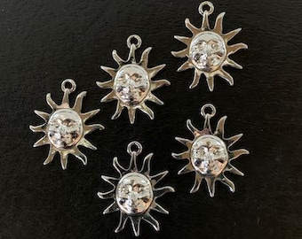 May include: Five silver sun charm pendants with a face on each. The charms are on a black background.