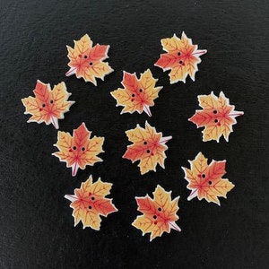 May include: Ten orange and yellow maple leaf buttons with a white background. The buttons are perfect for fall crafts and projects.