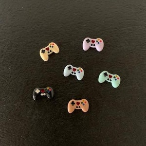 May include: Six miniature plastic game controllers in various colors, including black, blue, pink, and beige. Each controller has a heart-shaped button in the center.