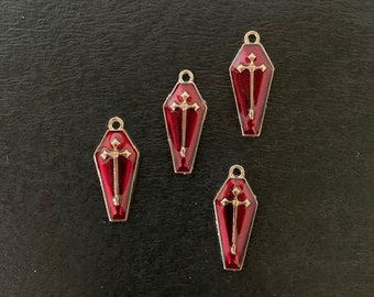May include: Four gold-colored metal charms shaped like red coffins with a gold cross inside.