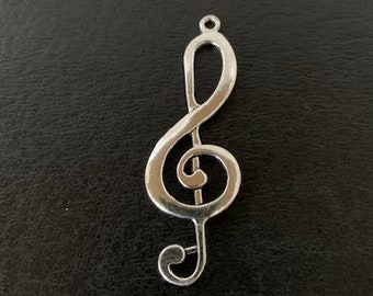 Puede incluir: Un colgante de plata con forma de clave de sol. El colgante es un diseño simple y elegante con un acabado liso y pulido.