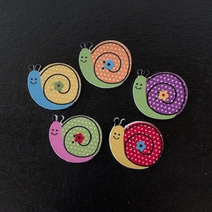 May include: Five wooden snail buttons with different colored shells and polka dot patterns. The snails have smiling faces and flowers on their shells.