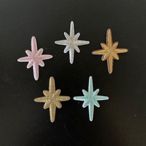 May include: Five embroidered iron-on patches in the shape of a starburst. The patches are in various colors, including silver, pink, gold, and light blue.