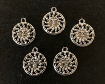 May include: Five silver sun charm pendants with a face in the center and rays around the face.