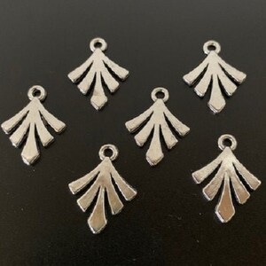 May include: Six silver metal charms in the shape of a stylized fan or leaf. Each charm has a small loop at the top for attaching to a necklace, bracelet, or other jewelry.