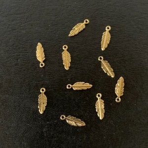 May include: A scattering of gold-toned metal feather charms with a loop at the top for attaching to jewelry or other crafts.