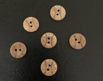 May include: Six wooden buttons with a baseball design. The buttons are beige with brown stitching and are arranged in a circle on a black surface.