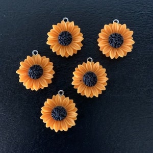 May include: Five yellow sunflower charms with black centers. Each charm has a silver loop for attaching to a necklace, bracelet, or other jewelry.