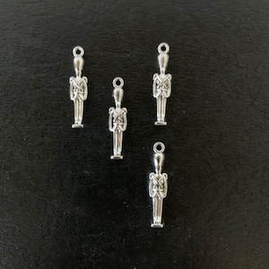 May include: Five silver-toned metal charms shaped like toy soldiers. Each charm has a detailed design and a loop for attaching to a necklace, bracelet, or other jewelry.
