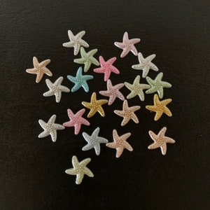 May include: A collection of pastel-colored starfish with glitter accents. The starfish are scattered on a black background.