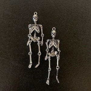 May include: Two silver skeleton charms, one larger than the other, with articulated limbs and a skull head.