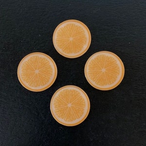 May include: Four orange citrus fruit slices with a white background, arranged in a square pattern on a black surface.