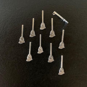May include: A collection of silver-toned metal charms shaped like broomsticks. The charms are arranged on a black surface.