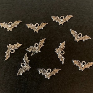 May include: Twelve silver bat charms with a rhinestone in the center. The charms are scattered on a black surface.