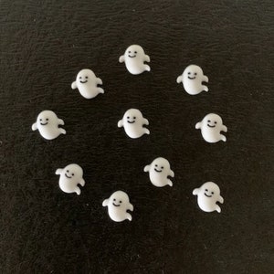 May include: Ten white ghost-shaped charms with smiling faces on a black background.