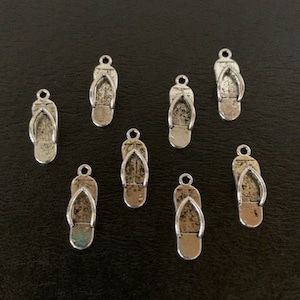 May include: Ten silver-toned flip flop charms. The charms are about 1 inch long and have a loop at the top for attaching to a bracelet or necklace.