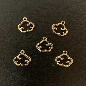 May include: Six gold-colored metal cloud charms. The charms are in the shape of a stylized cloud with a hole at the top for hanging.