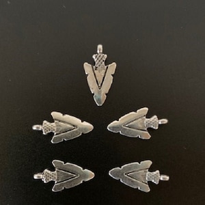 May include: Five silver arrowhead charms with a decorative design. The arrowheads are about 1 inch long and have a loop at the top for attaching to jewelry or other crafts.