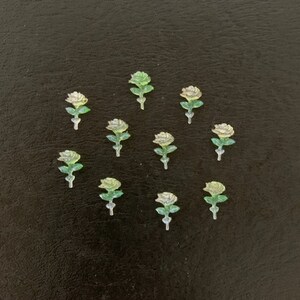 May include: Twelve white and green plastic rose flower embellishments on a black background.