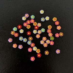May include: Assortment of colorful plastic flower embellishments. The flowers are in various shades of pink, yellow, orange, red, green, and blue.