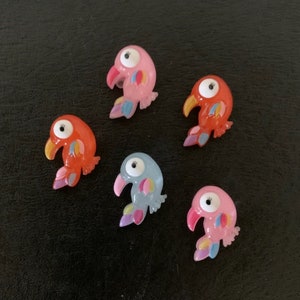 May include: Five colorful plastic bird buttons with googly eyes. The birds are pink, orange, blue, and pink. The buttons are about 1 inch in diameter.