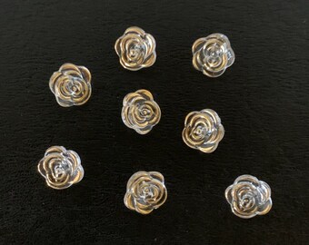 May include: Nine clear glass rose-shaped buttons with gold trim. The buttons are arranged in a grid pattern on a black surface.