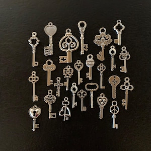 May include: A collection of 22 silver-toned skeleton keys with various designs, including hearts, swirls, and a peace sign. The keys are arranged in a random pattern on a black background.