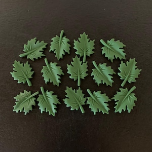 May include: A collection of 15 green felt maple leaves. The leaves are arranged in a semi-circle on a black background.