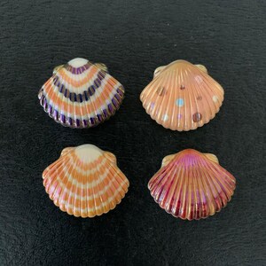 May include: Four decorative seashell ornaments in shades of orange, purple, and pink. Each shell has a unique pattern and iridescent finish. The shells are arranged on a dark surface.