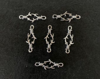 May include: Six silver-toned metal charms shaped like barbed wire. The charms are arranged in two rows of three. The charms are all the same size and shape.