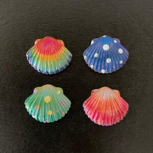 May include: Four decorative seashells with painted designs. One shell features a rainbow pattern, another is blue with white polka dots, a third is green with yellow and pink dots, and the last is red and orange.