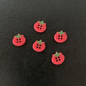 May include: Six red tomato-shaped buttons with green stems and four black buttonholes. The buttons are arranged on a dark surface. These decorative buttons are ideal for sewing and craft projects.