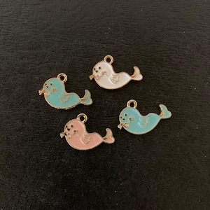 May include: Four colorful seal charms with gold-colored accents. The seals are in shades of blue, white, and pink. Each charm has a small loop at the top for attaching to jewelry or other crafts. The charms are on a dark background.