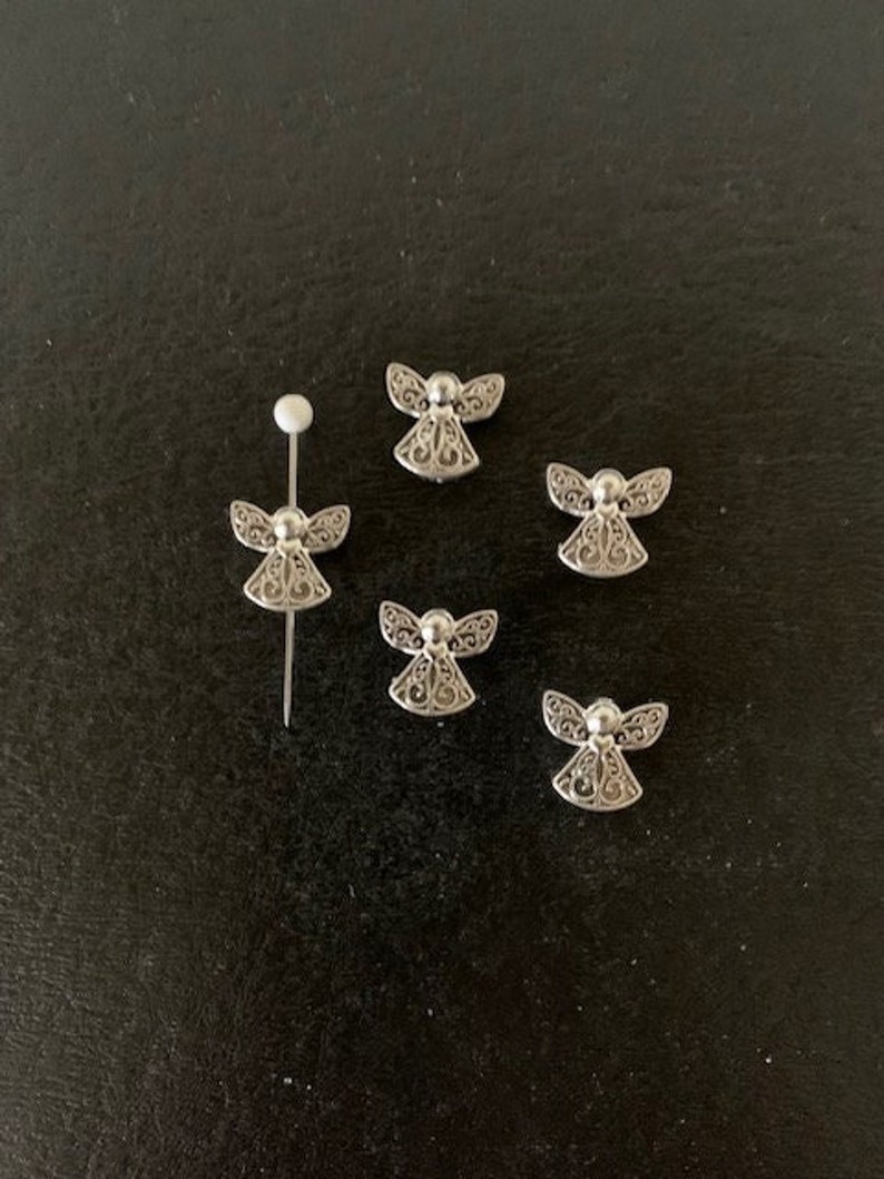 May include: Five silver angel charms with intricate designs. The charms are small and delicate, perfect for adding a touch of whimsy to jewelry or crafts.