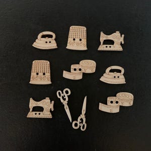 May include: A set of nine wooden buttons featuring sewing-themed designs, including a thimble, a sewing machine, an iron, and a measuring tape. The buttons are all made of natural wood and have a light brown color.