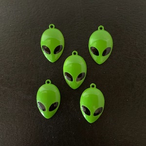 May include: Five green alien head charms with black eyes. The charms are made of metal and have a shiny finish.
