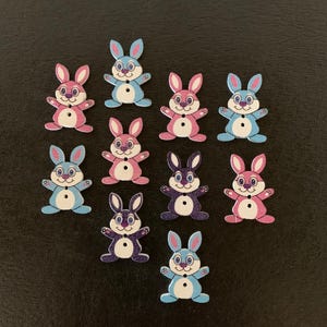 May include: Ten wooden bunny buttons in various colors, including pink, blue, and purple. Each button has a white face with black eyes and a black nose.