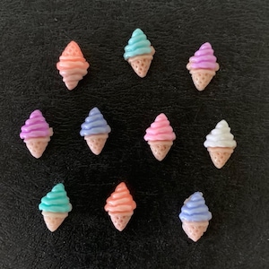 May include: A collection of ten miniature ice cream cone charms. Each charm features a waffle cone base topped with swirled ice cream in various pastel colors, including pink, blue, purple, and orange. The charms are arranged on a dark surface.