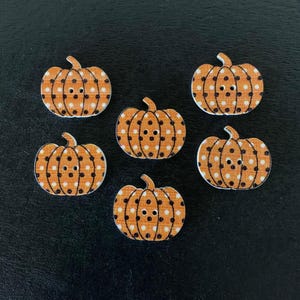 May include: Six wooden pumpkin-shaped buttons. Each button is orange with white polka dots and a small stem. The buttons have two holes for sewing. Perfect for fall and Halloween crafts.