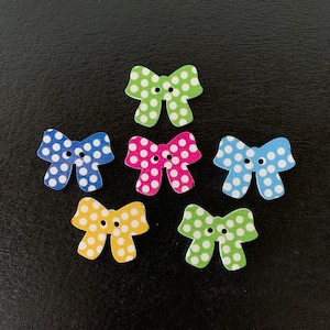 May include: Six wooden bow-shaped buttons with white polka dots. The buttons are in various colors: green, blue, pink, yellow, and light green.
