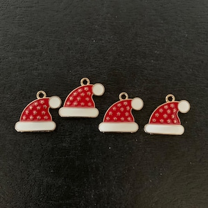 May include: Four Christmas-themed charms in the shape of Santa hats. Each hat is red with white accents and a gold-colored loop at the top. The hats have a white trim and a white pom-pom.