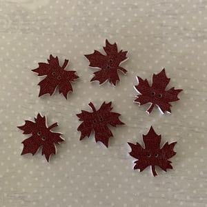 May include: Six burgundy leaf-shaped buttons with white edges and two holes each. These decorative wooden buttons are ideal for sewing, crafting, or adding a seasonal touch to clothing and accessories.