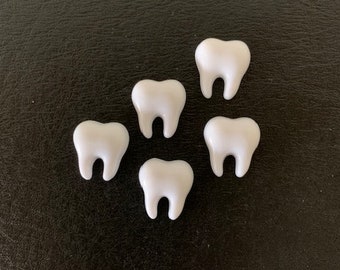 May include: Five white tooth-shaped ceramic buttons. The buttons are arranged in a semi-circle on a black surface.