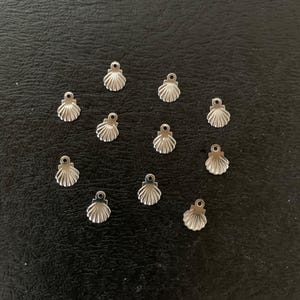 Puede incluir: Un conjunto de 12 abalorios de concha de mar de metal plateado. Los abalorios son peque&ntilde;os y delicados, con un dise&ntilde;o de concha de mar detallado. Son perfectos para a&ntilde;adir un toque de encanto n&aacute;utico a joyas o manualidades.