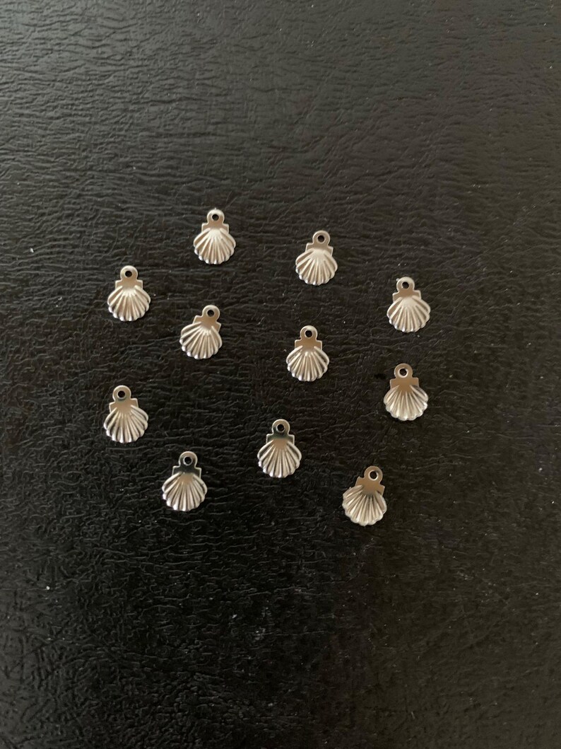 Puede incluir: Un conjunto de 12 abalorios de concha de mar de metal plateado. Los abalorios son peque&ntilde;os y delicados, con un dise&ntilde;o de concha de mar detallado. Son perfectos para a&ntilde;adir un toque de encanto n&aacute;utico a joyas o manualidades.