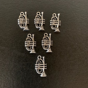 May include: Eight silver trumpet charms, each with a detailed design. The charms are small and perfect for adding a musical touch to jewelry or crafts.