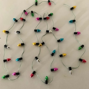 May include: A string of colorful Christmas lights with bulbs in various colors, including red, green, blue, silver, and gold. The lights are strung on a thin, silver-green wire. The bulbs are small and teardrop-shaped.