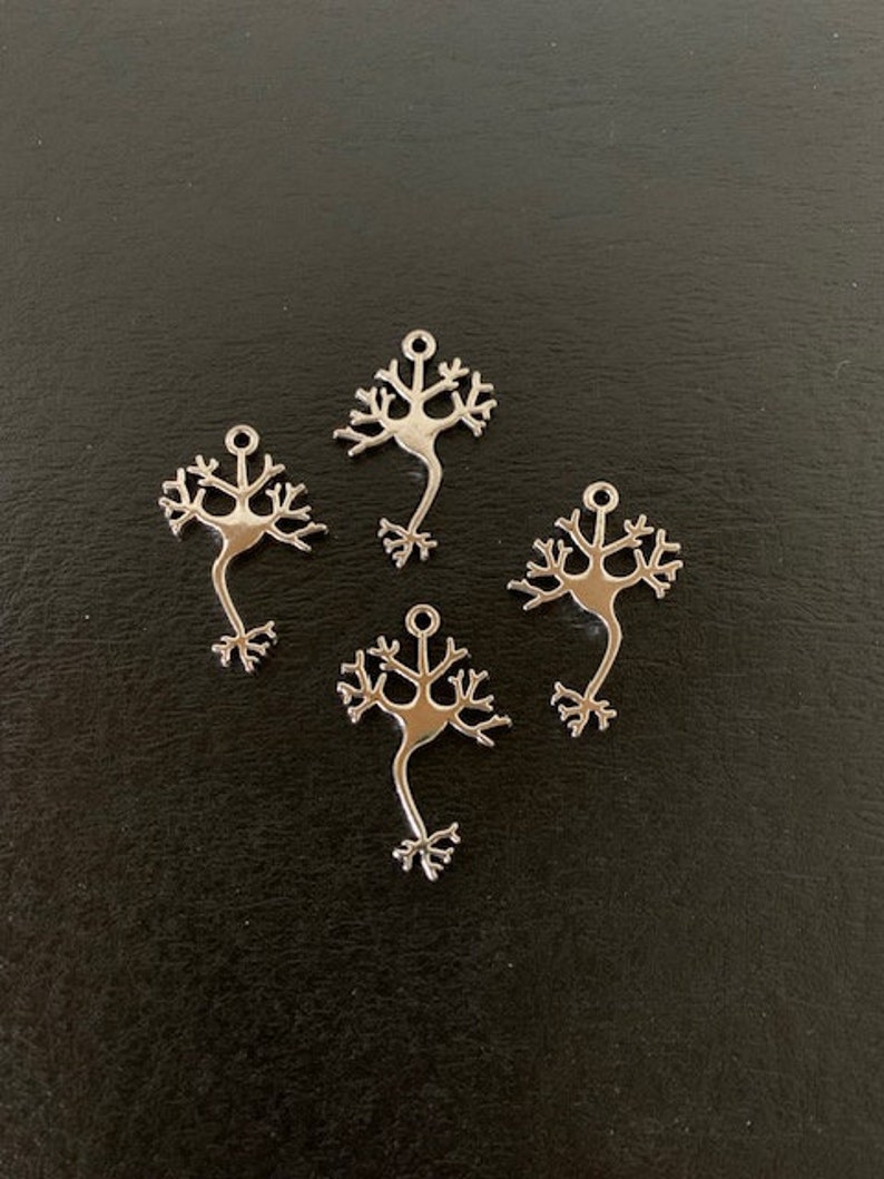 K&ouml;nnte beinhalten: Vier silberne Neuronen-Anh&auml;nger, jeder mit einem detaillierten Design eines Neurons, einer Art Nervenzelle. Die Anh&auml;nger sind auf einer dunklen Oberfl&auml;che angeordnet.