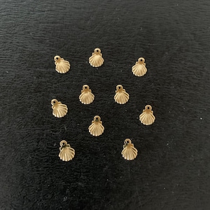 May include: A collection of twelve gold-colored seashell charms, arranged in a heart shape on a black background.