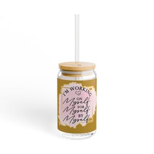 May include: A gold glass tumbler with a bamboo lid and a clear straw. The tumbler has a pink and gold design with the text "I'm working on myself for myself by myself".